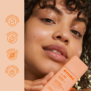 Femme tenant une bouteille de crème solaire Byoma avec les caractéristiques du produit sur le côté.