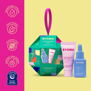 Coffret de produits de soin BYOMA avec boîte verte et flacons roses et bleus sur fond jaune